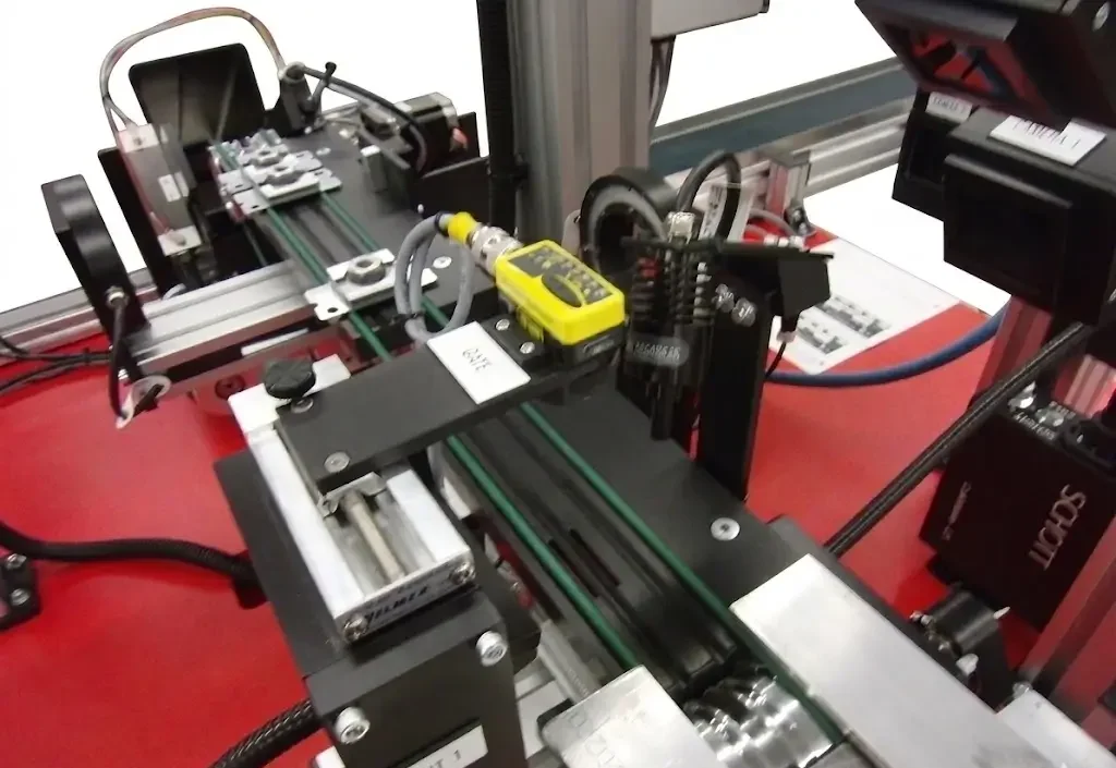 Industrial test/inspection rig with sensors, cabling, and a linear slide assembly mounted on an aluminum extrusion frame.
