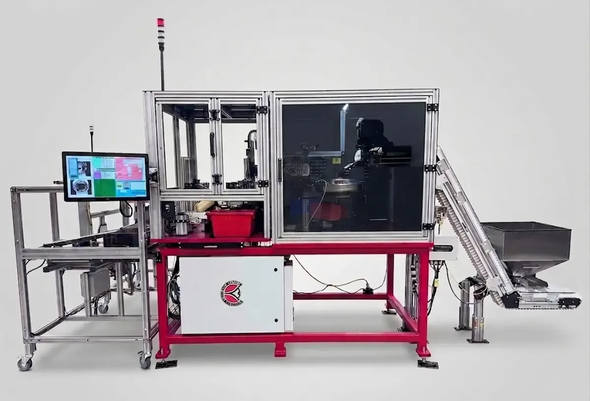Wide view of an enclosed automation cell with HMI screen on the left and an inclined conveyor feed on the right.